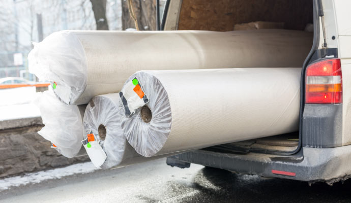 four large rolled-up rugs secured with white plastic in the back of a delivery van