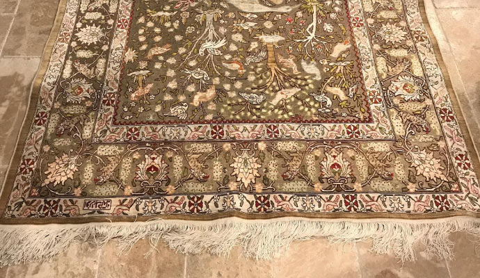  a detailed silk rug laid out on a tiled floor.